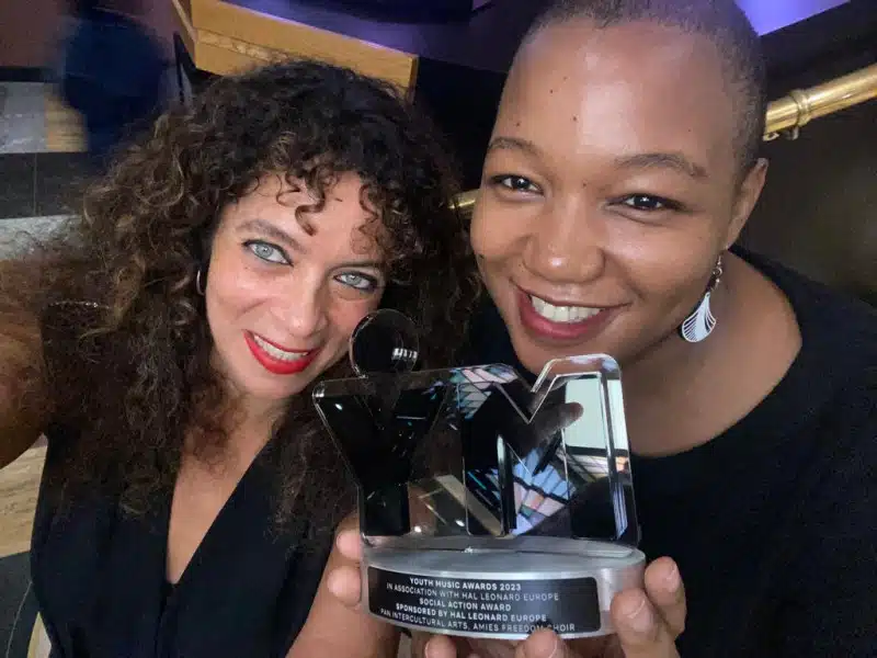 Two women smiling and holding a shiny black YM award trophy. The woman on the right holds the award, whilst both look towards the camera in a celebratory atmosphere.
