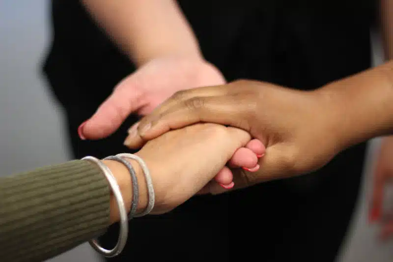 Close-up of three hands, each from different people, gently holding one another in a supportive gesture, symbolising comfort, unity, and compassion.