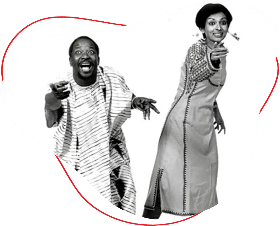 A man in traditional striped attire and a woman in a long, embroidered dress smile and gesture energetically against a white background.