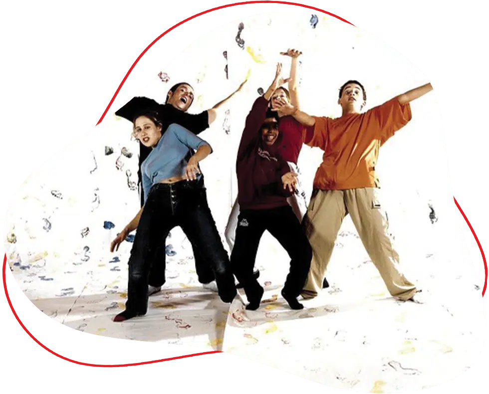 Four people, dressed casually, pose energetically and playfully in front of a white background with colourful markings, each extending their arms and legs in different directions as if dancing or having fun.