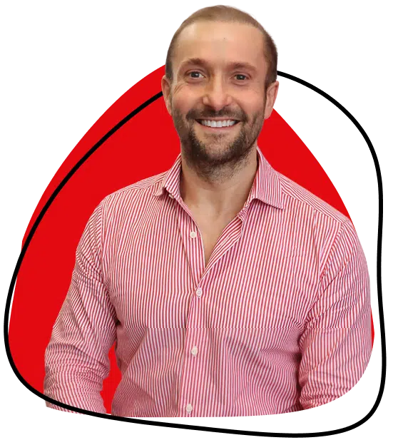 A man with short hair and a beard smiles, wearing a red and white striped button-down shirt. He stands in front of a red abstract shape with a black outline.