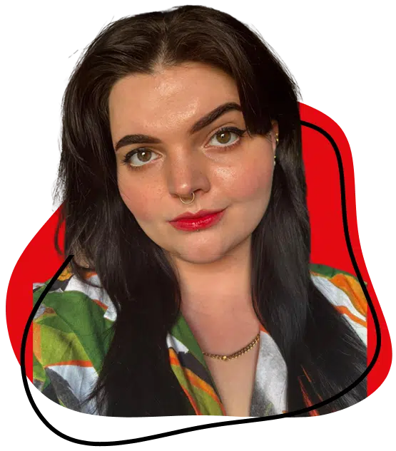 A person with long dark hair, bold eyebrows, and a septum piercing faces the camera, wearing a colourful patterned shirt and a gold necklace, with a red and black abstract background.