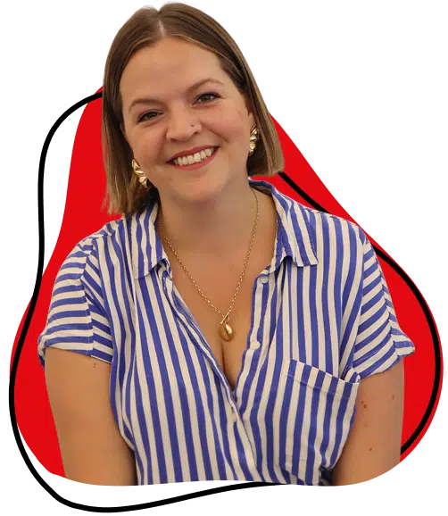 A smiling woman with short brown hair wearing a blue and white striped shirt, gold earrings, and a gold necklace, posed in front of a red and black abstract shape on a light background.