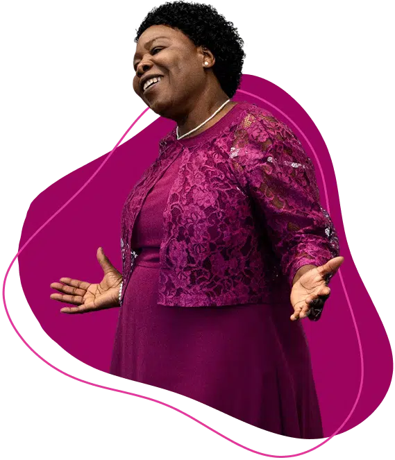 A woman in a vibrant magenta lace dress and jacket smiles warmly with her arms open, standing in front of an abstract magenta background shape.