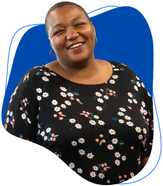 A person with short hair wearing a black top with a white floral pattern, smiling in front of a blue abstract background shape.