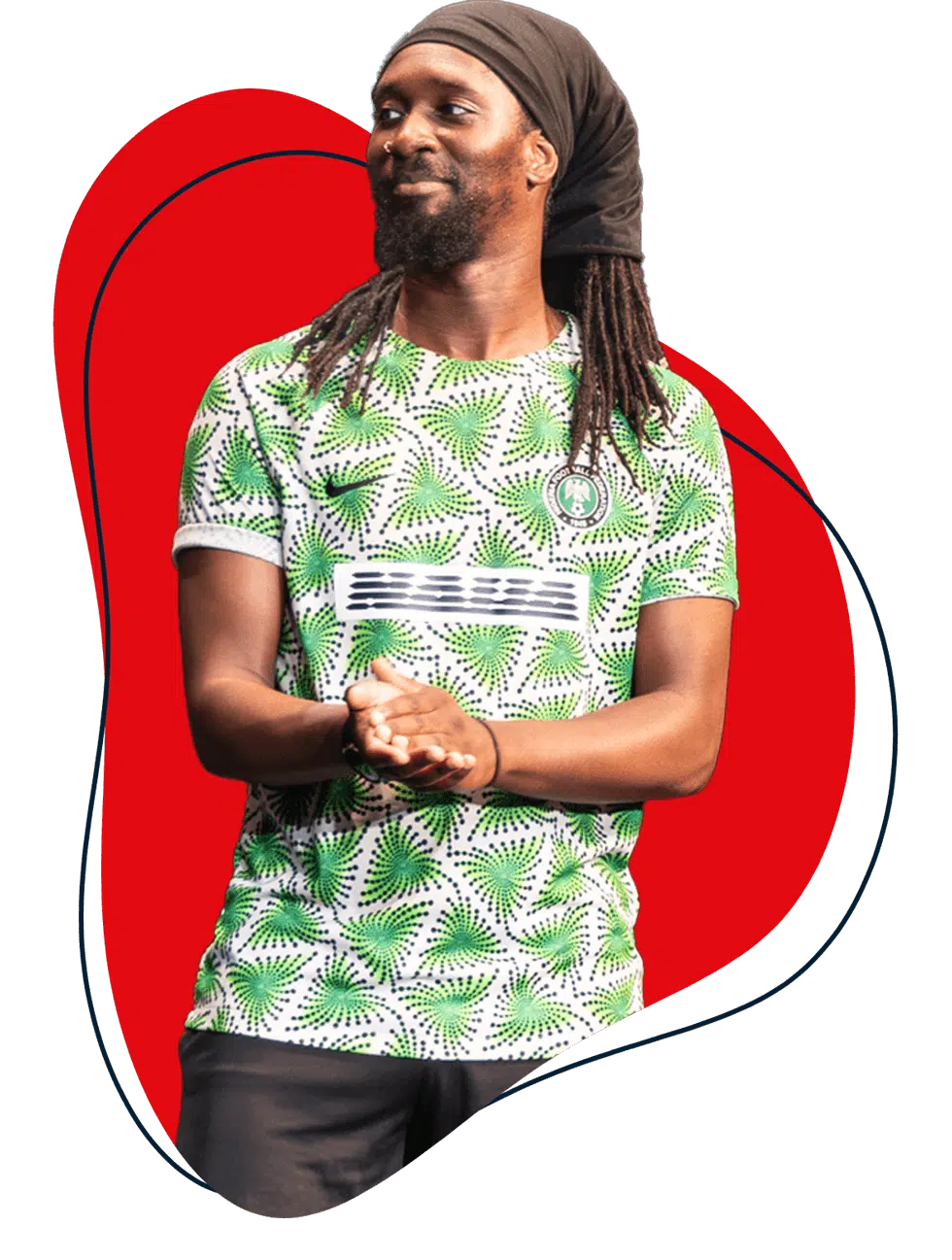 A man with long dreadlocks wearing a green and white patterned shirt stands with hands clasped, smiling. The background features a bold red abstract shape outlined in blue.