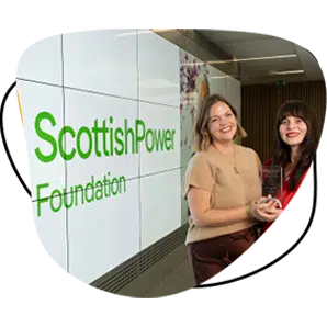 Two women smiling and holding an award stand in front of a large digital screen displaying the ScottishPower Foundation logo.