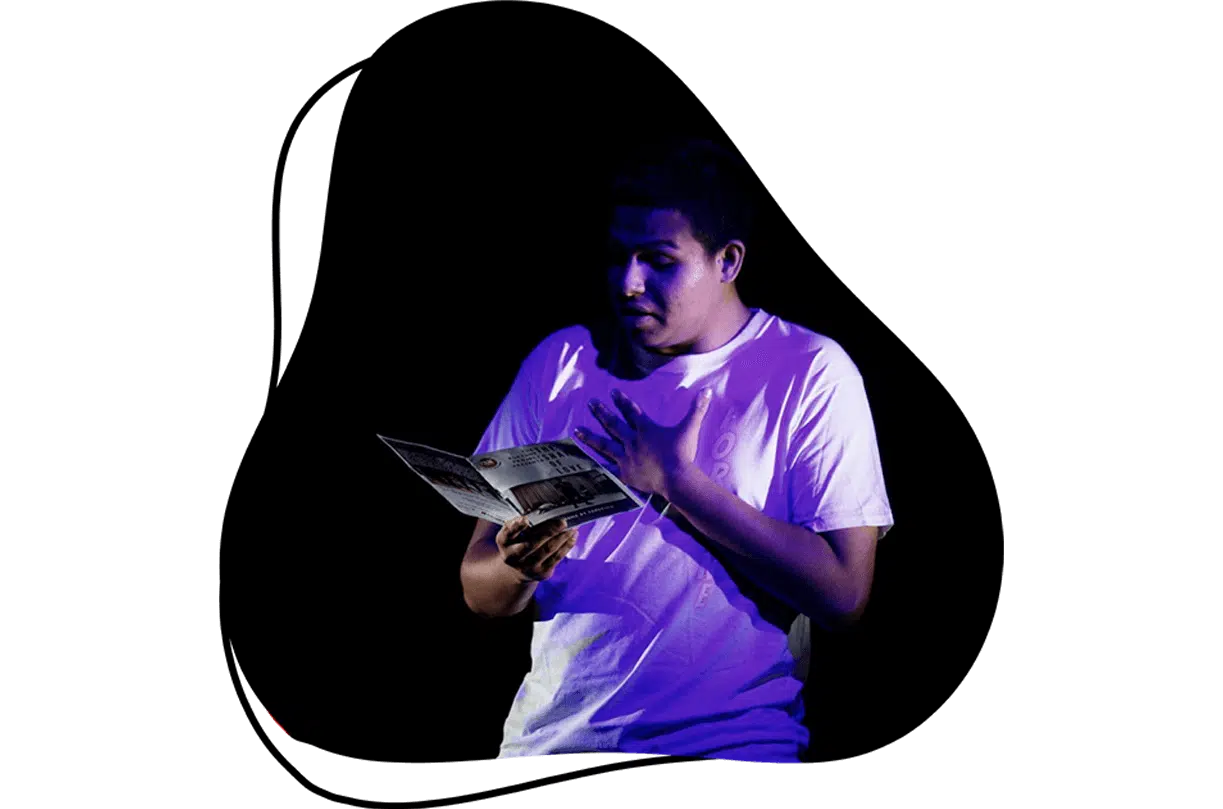 A person in a white T-shirt stands under purple lighting, holding and reading a booklet with one hand on their chest, set against a black abstract background.