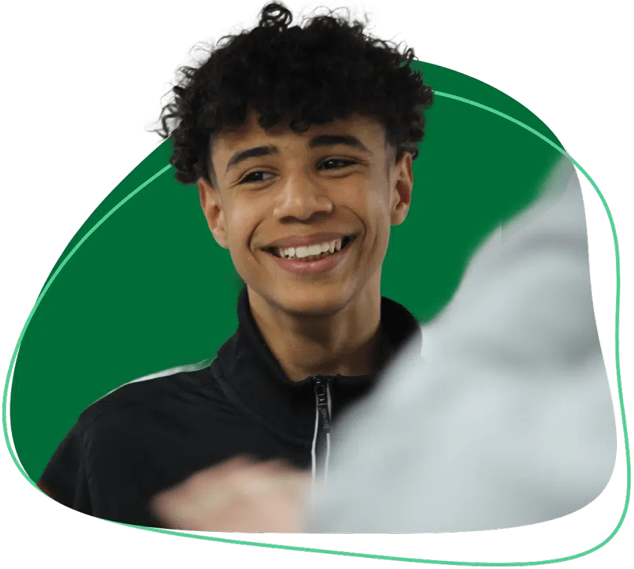 A young person with curly dark hair and a black zip-up jacket smiles, standing in front of a green abstract background shape.