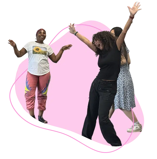 Three people stand in front of a pink shape. One person wears a white T-shirt and colourful trousers, another in black dances with arms raised, and a third in a floral dress stands behind them. All appear to be having fun.