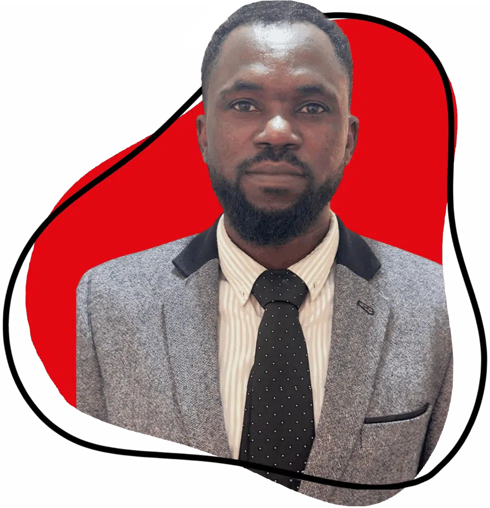 A man with a beard wearing a grey suit, white striped shirt, and black polka dot tie stands in front of a red background outlined by a black abstract shape.